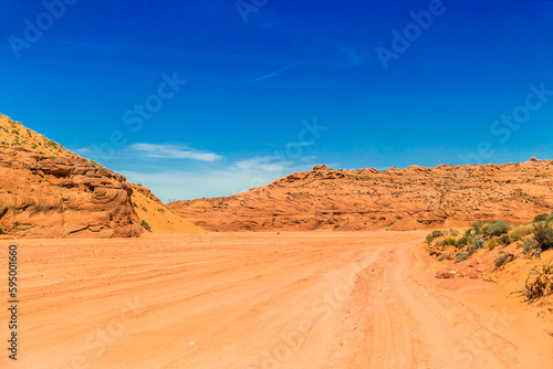 Dusty and unpaved road through the arid and dry desert. Desert with sand dunes and blue sky. 