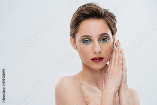 young woman with shimmery eye makeup and short hair standing with praying hands isolated on grey.
