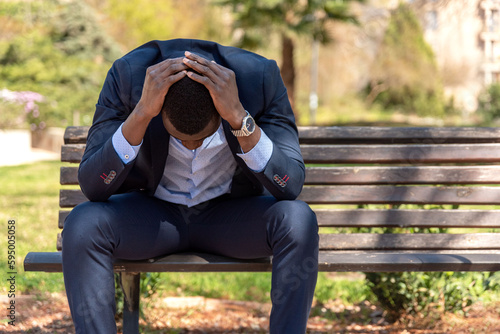 Black disappointed male entrepreneur sitting on bench in park photo