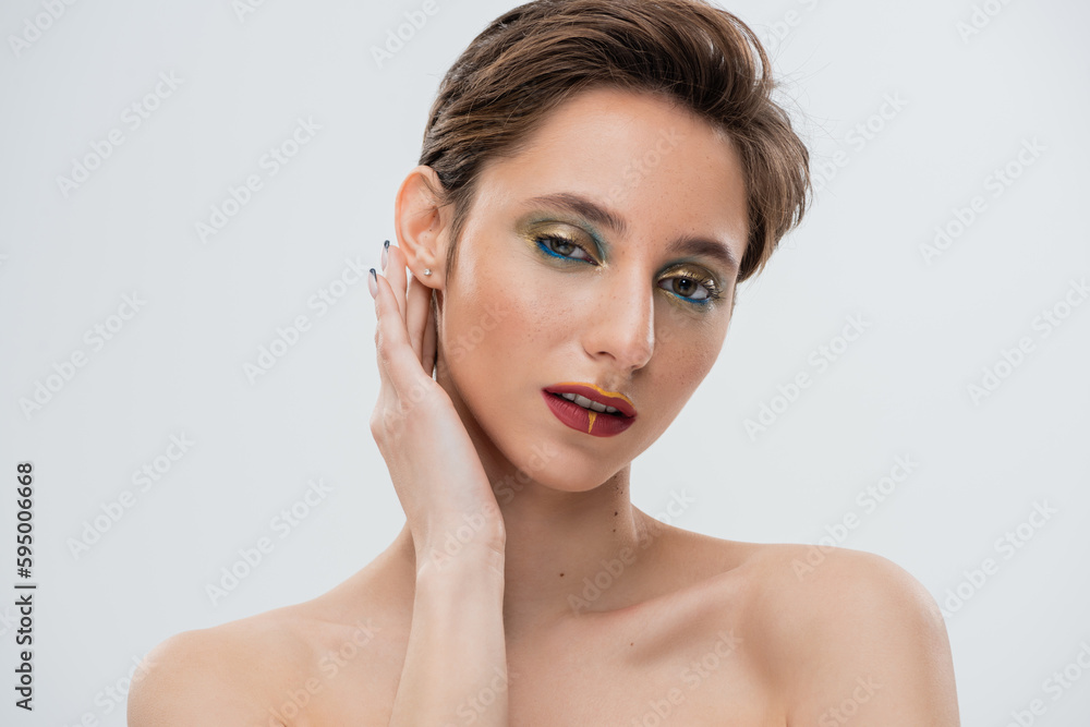 portrait of young model with bright makeup fixing shirt hair and looking at camera isolated on grey. portrait of young model with bright makeup fixing shirt hair and looking at camera isolated on grey.