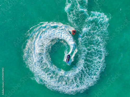 Aerial top view of a speed boat navigating the open ocean performing thrilling tricks and maneuvers © Babyone Productions/Wirestock Creators