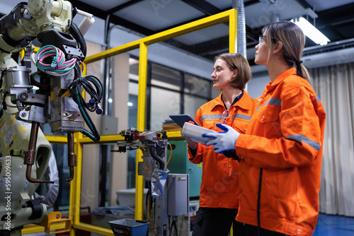 Girl engineer commissioning operating programming and looking at robot machine in the factory