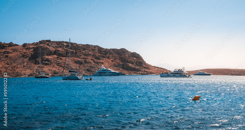 Landscape featuring a body of water surrounded by hills and rocky terrain, with boats sailing on