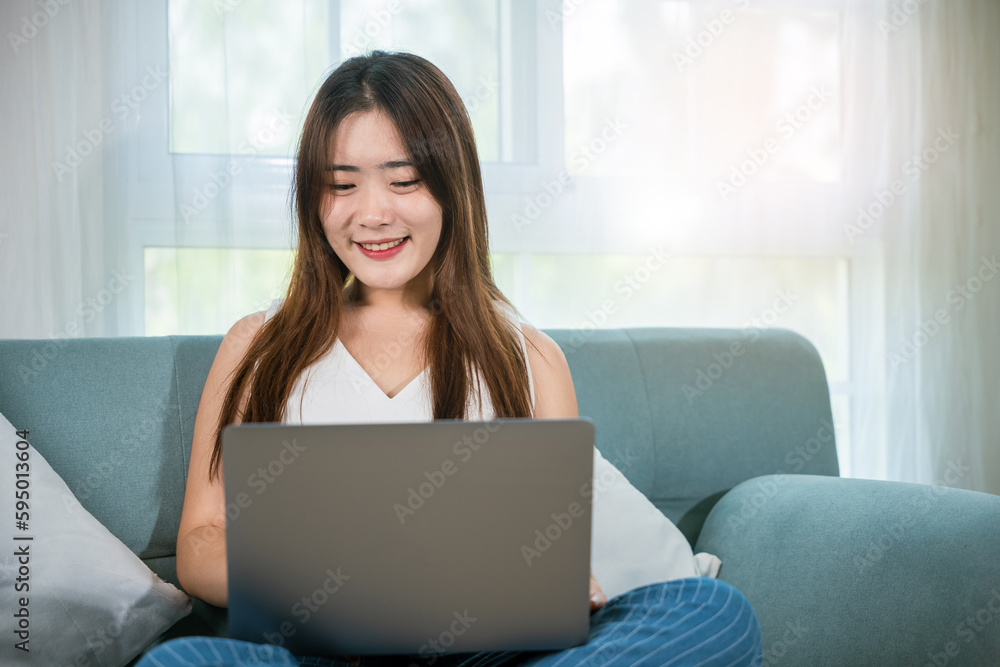 Happy woman browsing through the internet during free time on laptop computer, Female smiling sit on sofa using laptop in living room at home, girl shopping or chatting online in social media network Happy woman browsing through the internet during free time on laptop computer, Female smiling sit on sofa using laptop in living room at home, girl shopping or chatting online in social media network