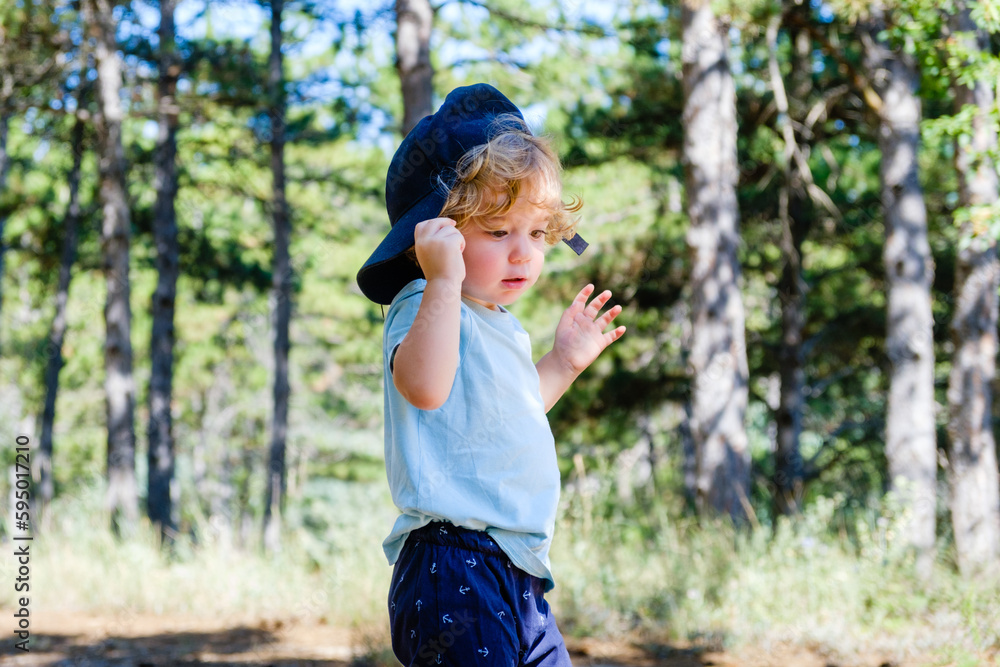 Blond preschooler with a baseball cap plays in the forest