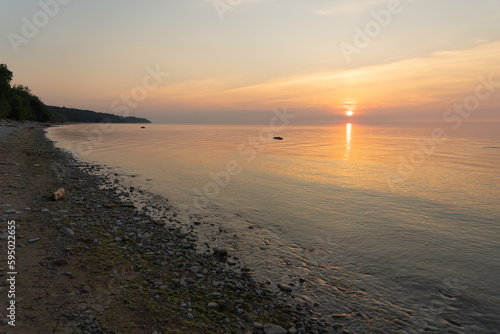 Summer sunset on the shore of the bay in Toila Oru Park. Orange clear sky. Ripples on the water from the wind. Pebbles on the shore. Natural background. Space for text. photo