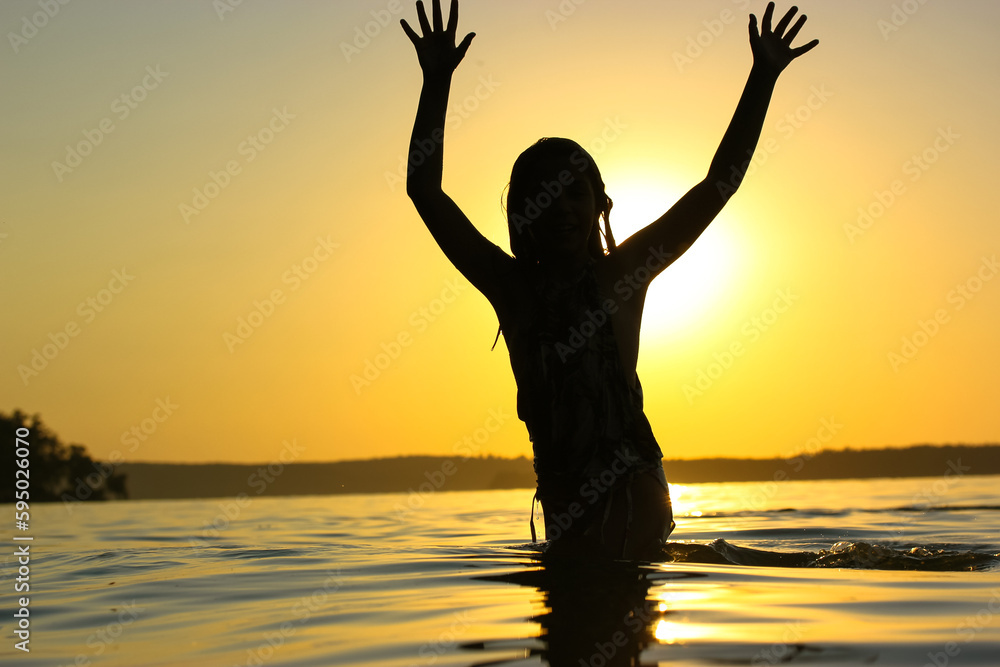 Silhouette of girl in a rive at sunset with hands up in the air. Summer vacation