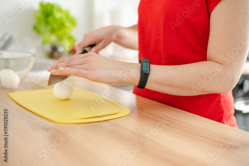 A woman in red cuts a boiled egg for salad on a yellow board. Focus on fingers.