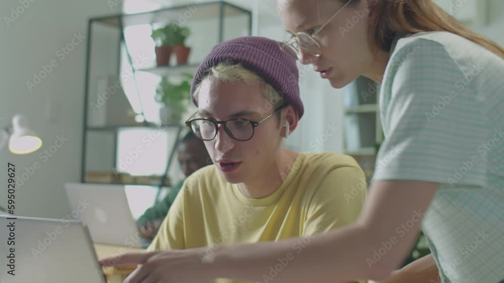 Young gen Z male and female colleagues talking about business project on laptop while cooperating at work in office Young gen Z male and female colleagues talking about business project on laptop while cooperating at work in office