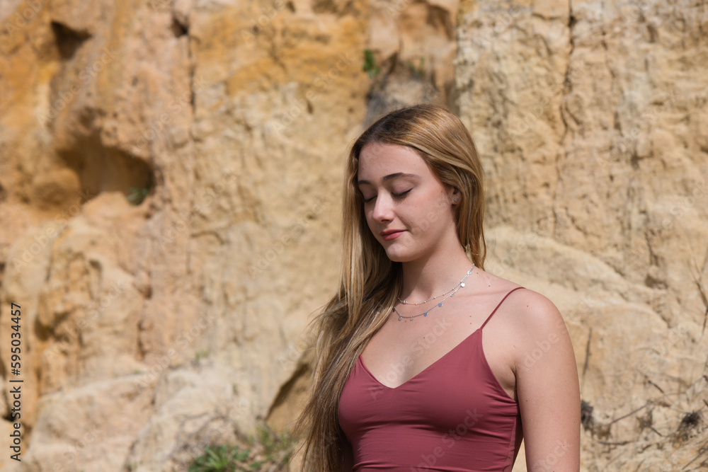pretty young woman in red summer dress is posing on the cliff. The woman makes different body expressions. In the background rocks and vegetation.