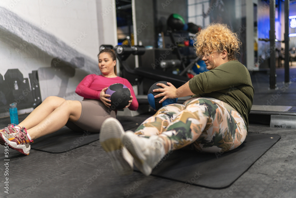 Two plus-size women workout and exercise with medicine ball at the gym. They're determined to achieve their goals and inspire others along the way. Two plus-size women workout and exercise with medicine ball at the gym. They're determined to achieve their goals and inspire others along the way.