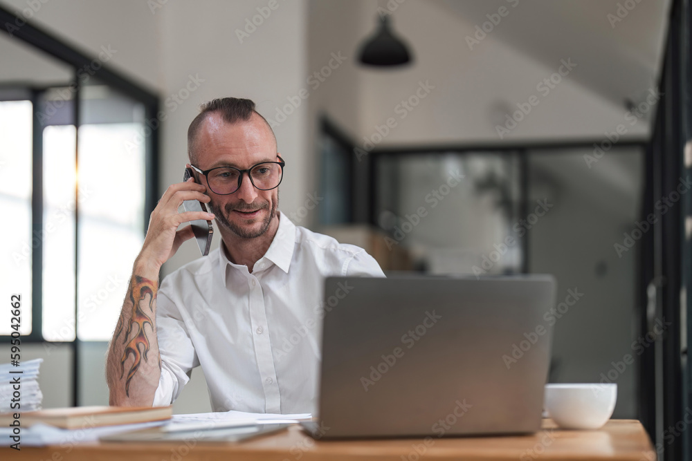 businessman talking on cell phone while working on computer in office businessman talking on cell phone while working on computer in office