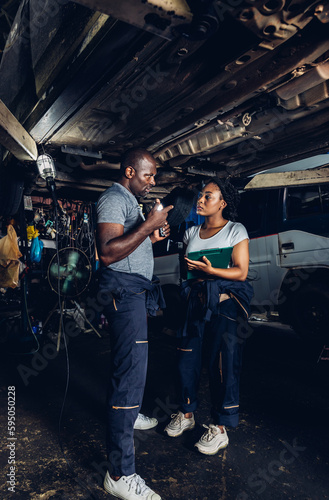 Professional Car Mechanic is Investigating Under a Vehicle on a Lift in Service. Auto Service Worker Checking Car Under Carriage Look For Issues. Car service technician check and repair customer car.