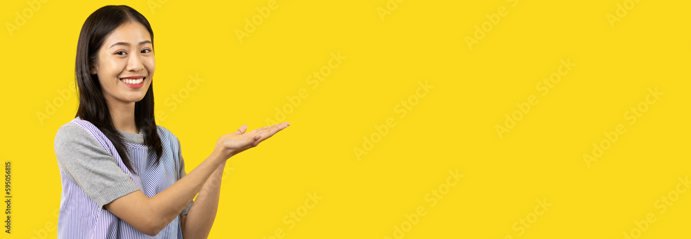 Εκτύπωση καμβά Asian woman with holding copyspace imaginary on the palm to insert an ad, Showing copyspace pointing, Showing her hand to present something on yellow background