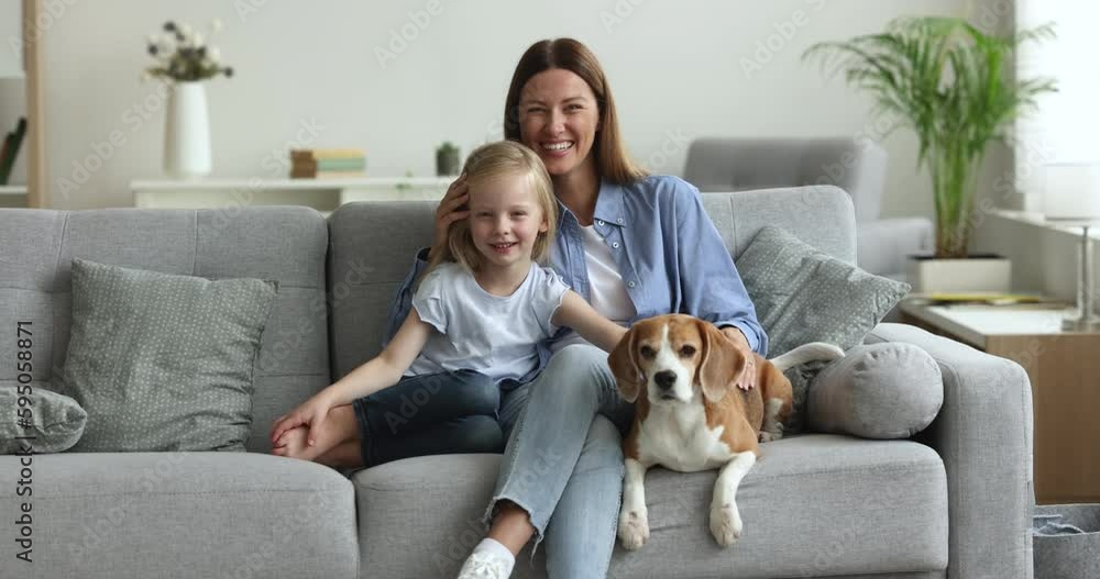 Cheerful young mother with 5s daughter and trained dog sitting on cozy couch in living room, loving parent hugging her child feeling love, enjoy happy motherhood, spend time threesome at modern home Cheerful young mother with 5s daughter and trained dog sitting on cozy couch in living room, loving parent hugging her child feeling love, enjoy happy motherhood, spend time threesome at modern home
