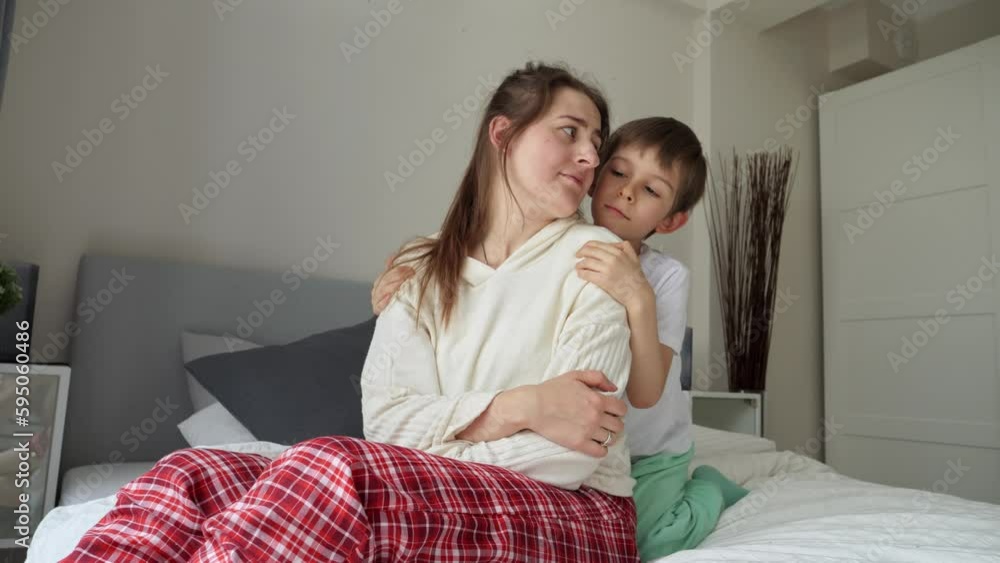 Little boy in pajamas hugging his sad mother on bed. Concept of loving family, parents and kids, love and support Little boy in pajamas hugging his sad mother on bed. Concept of loving family, parents and kids, love and support