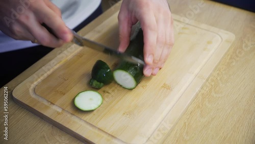 High angle of a person cutting the green zucchini on the wooden chopping board photo