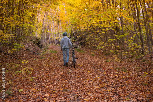 Young fit man walking with bike through park forest alley fall tunnel made of colorful tree brunches. Fall colors scene. Recreational sport  hiking  biking and cycling concept. Selective focus. 