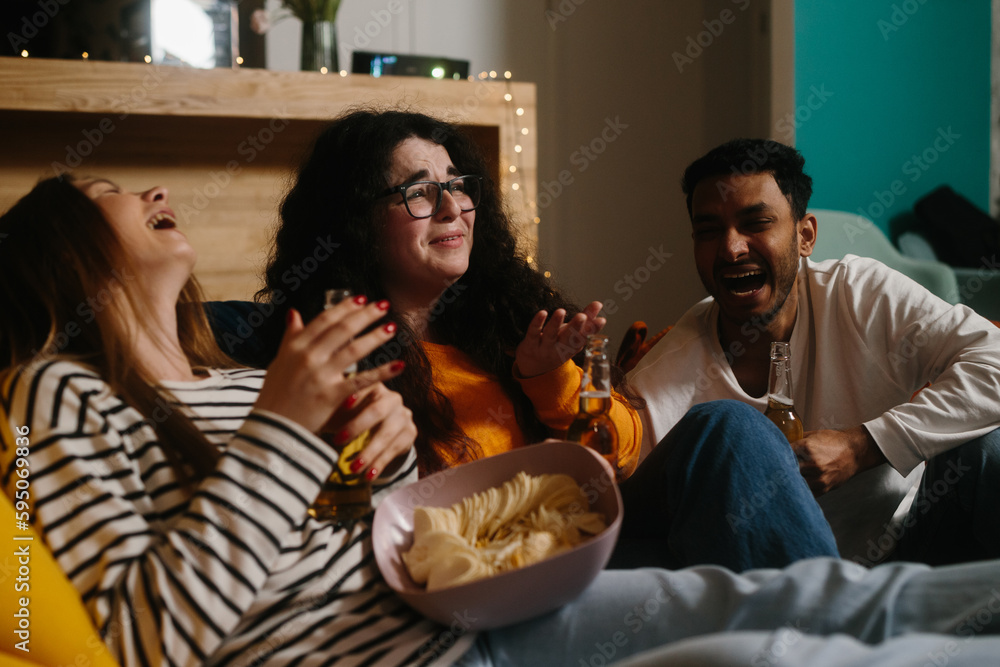 A group of friends watch a comedy movie sitting on soft bean bags with drinks and snacks.