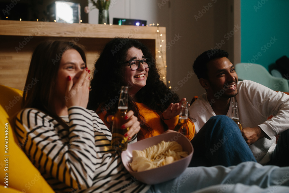 A group of friends watch a comedy movie sitting on soft bean bags with drinks and snacks. A group of friends watch a comedy movie sitting on soft bean bags with drinks and snacks.