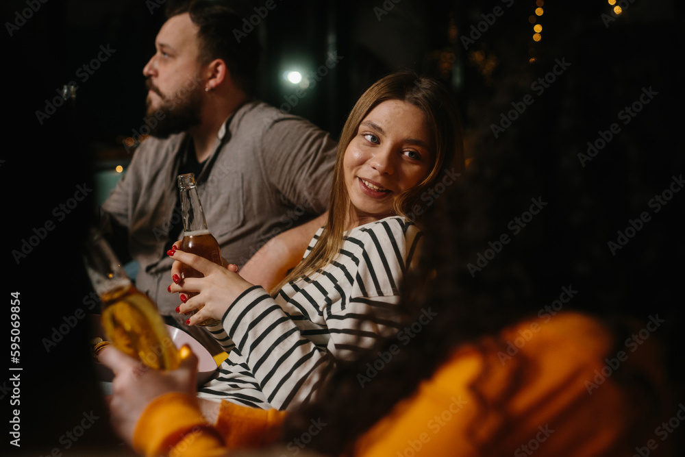 A group of friends have fun together in a cafe in the evening, drink beer and chat.