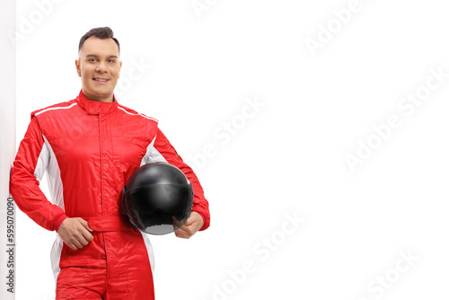 Racer in a red suit leaning on a wall and holding a black helmet