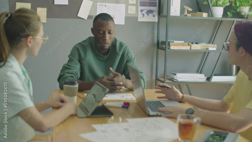 Young black man telling agenda to gen Z Caucasian colleagues while having business meeting with team in office Young black man telling agenda to gen Z Caucasian colleagues while having business meeting with team in office