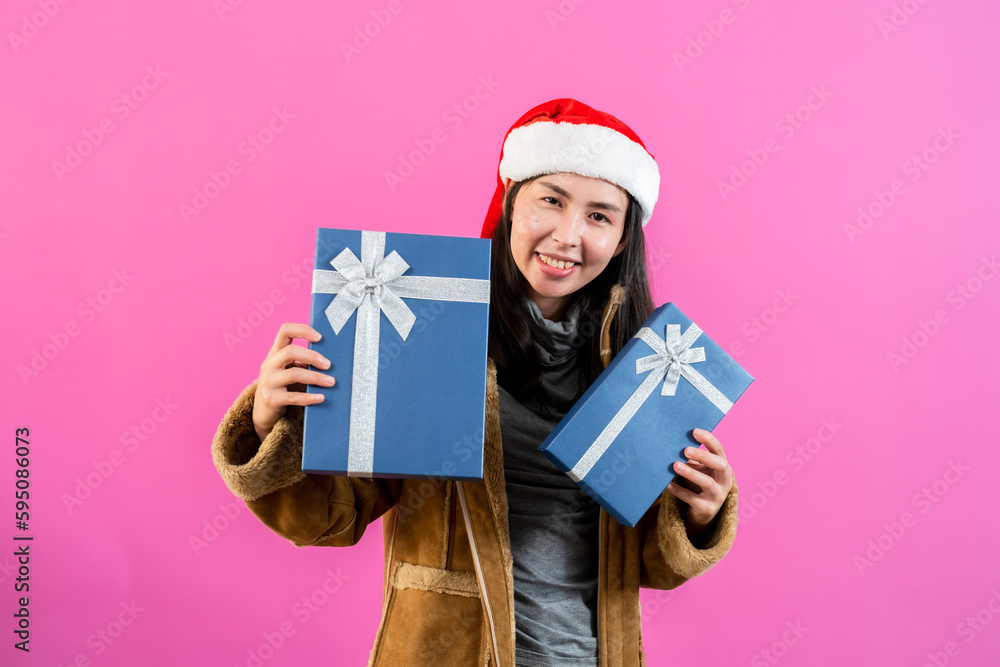 portrait, Asian woman wearing long-sleeved outerwear and Christmas hat, holding two gift boxes with two hands held out happily receiving two boxes presents, Isolated indoor studio on pinkbackground. portrait, Asian woman wearing long-sleeved outerwear and Christmas hat, holding two gift boxes with two hands held out happily receiving two boxes presents, Isolated indoor studio on pinkbackground.