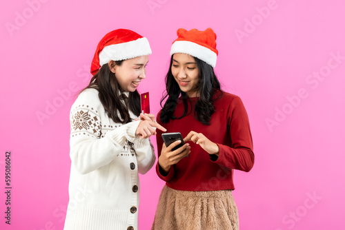 portrait, Two young Asian women in long sleeves christmas hats during christmas season, opening map see travel route festival on mobile phone, Isolated indoor studio on pink background.