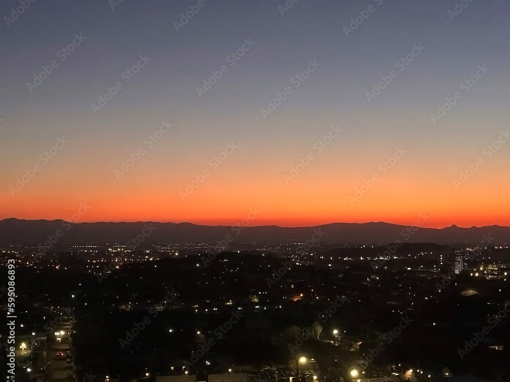 Aerial view of city center in the night lights at sunset and mountain on the horizon