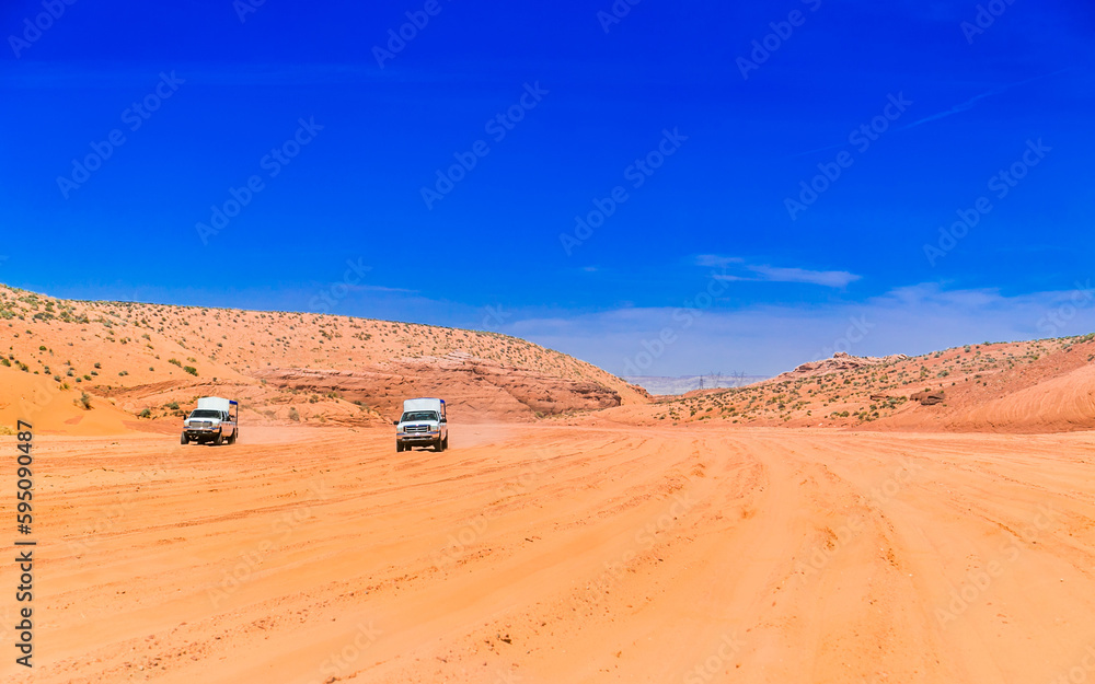 Two jeeps 4x4 moving across the sandy road. Trip to Antelope Canyon. A picture with a blue sky and a broken unpaved road in the desert. Dusty and unpaved road through the arid and dry desert. Two jeeps 4x4 moving across the sandy road. Trip to Antelope Canyon. A picture with a blue sky and a broken unpaved road in the desert. Dusty and unpaved road through the arid and dry desert.