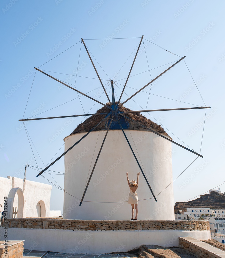Young woman standing in front of a windmill. Ios, Greece.