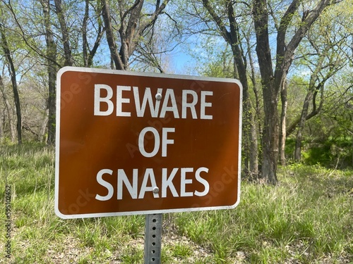 Rectangular sign featuring "BEWARE OF SNAKES" with a forest on the background