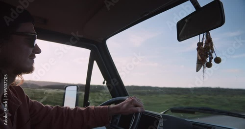 Details of a young man driving in his vintage van towards the cliffs and coastline of the Algarve to watch the upcoming sunset with blue sky in background and steering wheel in his hands, Portugal