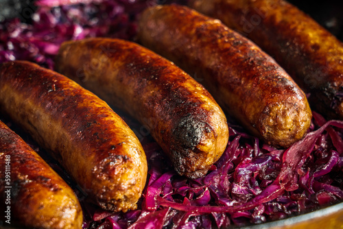 Beer-braised bratwurst sausages with red cabbage and onion in a cast-iron skillet.