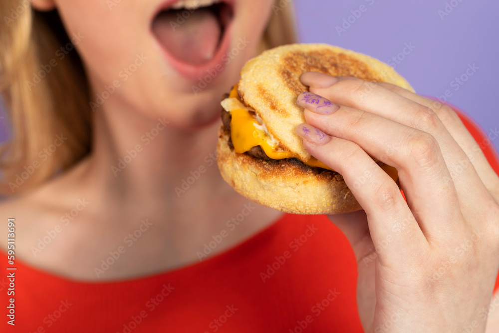 Excited surprised pretty girl eats fast food, cheap burger, holding fries and burger, open mouth. fast food and unhealthy diet. isolated on purple background. Excited surprised pretty girl eats fast food, cheap burger, holding fries and burger, open mouth. fast food and unhealthy diet. isolated on purple background.