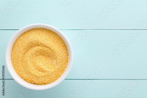 Raw coarsely ground cornmeal or polenta in white bowl, photographed overhead on blue wood with copy space on the side (Selective Focus, Focus on the cornmeal) photo