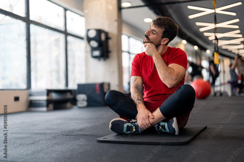 Athletic man in sports clothes warming up for sports training in gym, stretching neck muscles before workout, sitting on exercise fitness mat. Athletic man in sports clothes warming up for sports training in gym, stretching neck muscles before workout, sitting on exercise fitness mat.