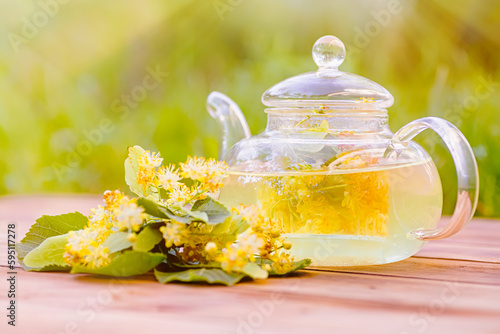 glass of refreshing linden tea with linden flowers on a wooden table in a garden