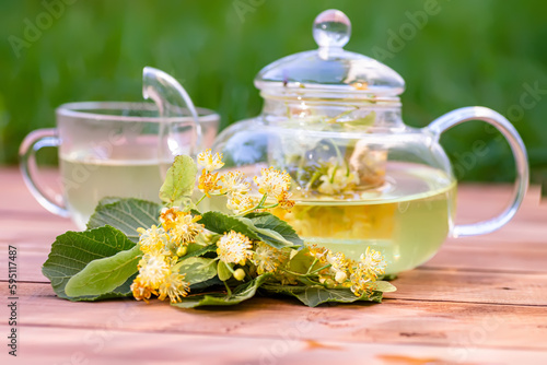 cup of hot linden tea with honey and linden flowers on wooden table in garden. golden color of tea and sweetness of honey and flower delicious and soothing drink.