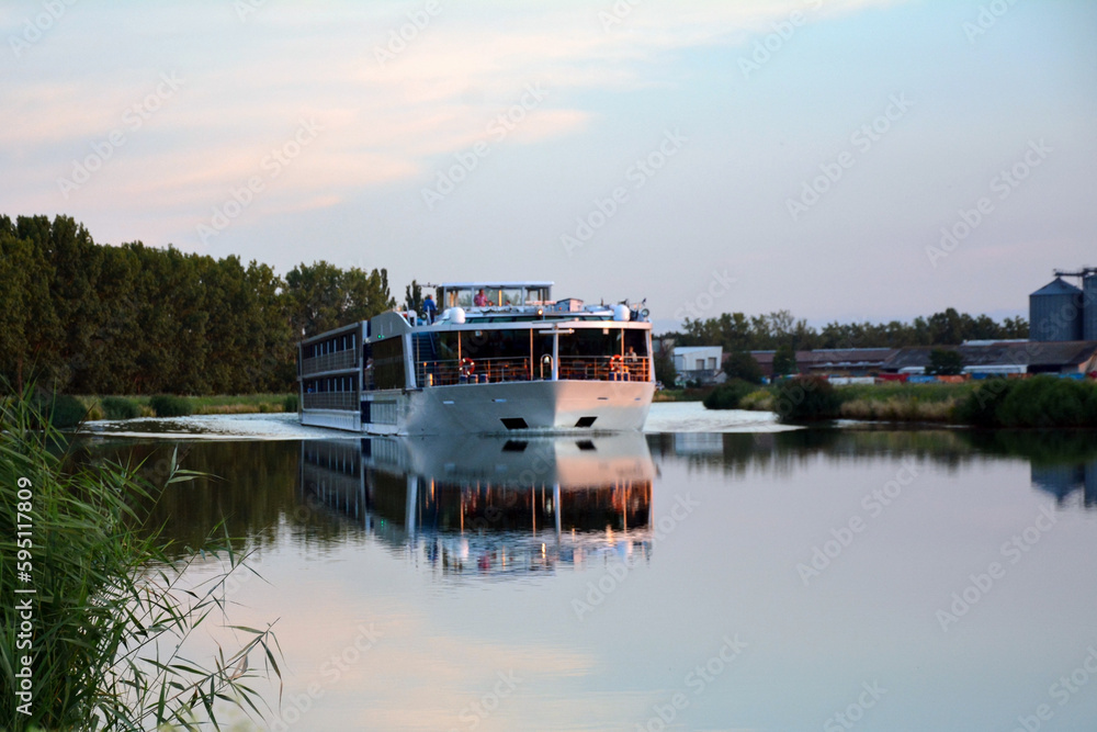 A large tourist passenger ship sails along the calm river between the banks A large tourist passenger ship sails along the calm river between the banks