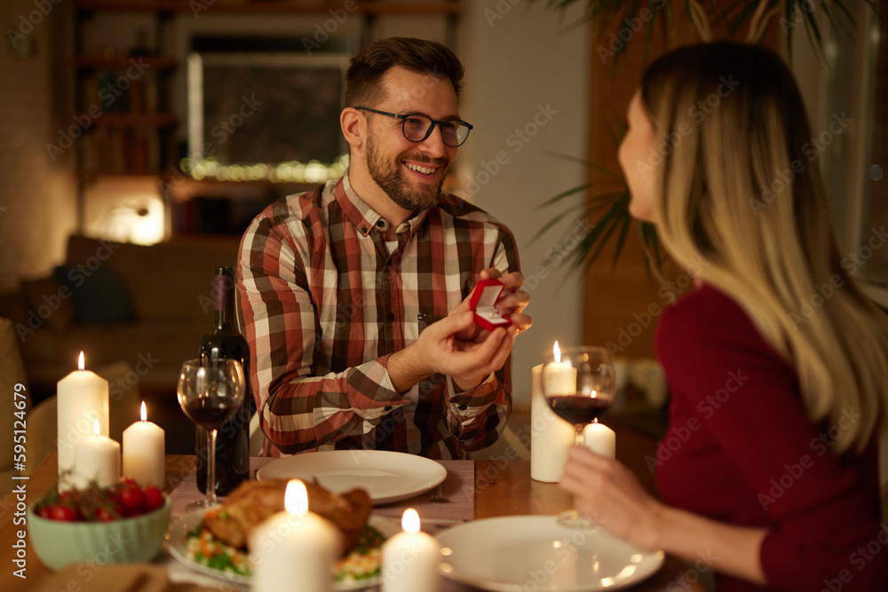 Delighted woman looking at her boyfriend while getting a marriage proposal over romantic dinner at home