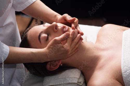 masseur doing facial massage to young woman on massage table. Concept of massage spa treatments. Close-up