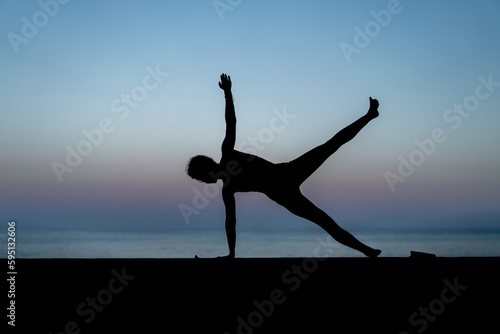 Silhouette de femme faisant du yoga devant la mer au coucher de soleil, posture Ardha Chandrasana (Half-Moon Pose - Demi-lune) photo