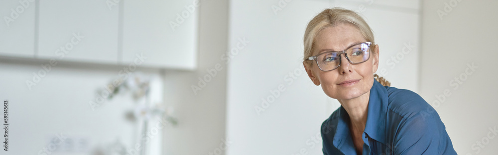 Mature businesswoman working from home, checking email using laptop computer and drinking coffee in the morning, standing in the kitchen