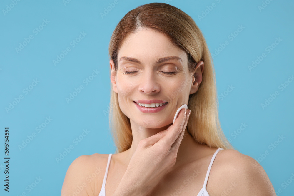 Beautiful woman removing makeup with cotton pad on light blue background Beautiful woman removing makeup with cotton pad on light blue background