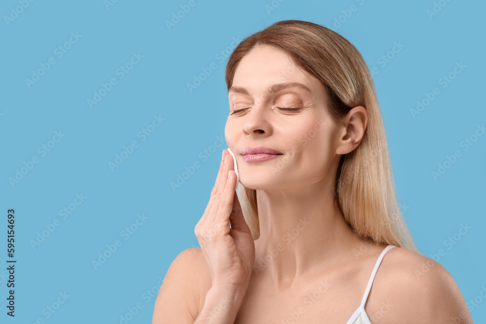 Beautiful woman removing makeup with cotton pad on light blue background, space for text Beautiful woman removing makeup with cotton pad on light blue background, space for text