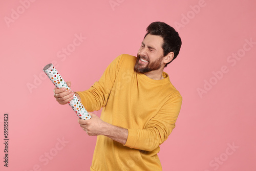 Emotional man with party popper on pink background