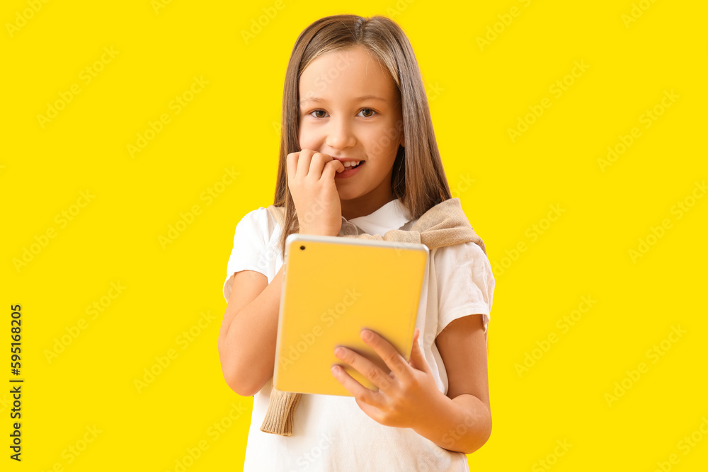 Little girl with tablet computer biting nails on yellow background Little girl with tablet computer biting nails on yellow background
