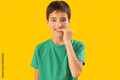 Little boy biting nails on yellow background